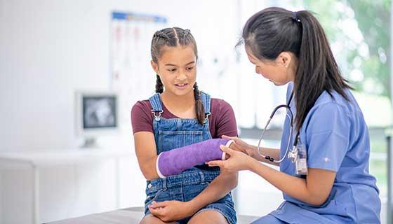Health care provider examining girl's arm in cast.