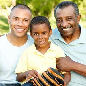 戴着棒球手套的孩子和他的父亲和祖父坐在一起，对着镜头微笑